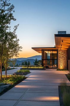 the entrance to a modern home at dusk with mountains in the background and trees on either side