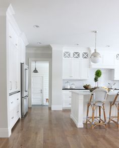 an open kitchen with white cabinets and wood flooring, along with two bar stools