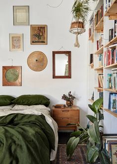 a bedroom with bookshelves, plants and pictures on the wall above the bed