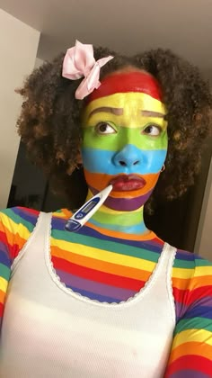 a woman with her face painted like a rainbow flag and holding a toothbrush in her mouth