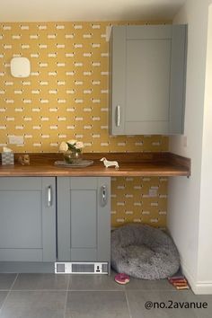 a dog bed in the corner of a room with yellow wallpaper and grey cabinets