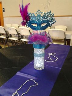 a purple table runner with a mask on top and beads in the middle, along with other decorations