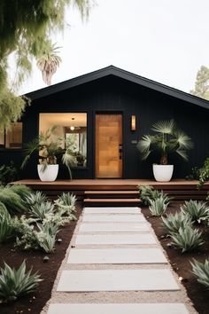 a black house with white steps leading up to the front door and plants on either side