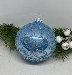 a blue ornament sitting on top of snow covered ground next to pine branches