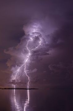 a large cloud filled with lots of lightning next to the ocean under a cloudy sky