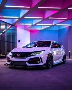 a white honda civic type car parked in front of a building with purple and blue lights