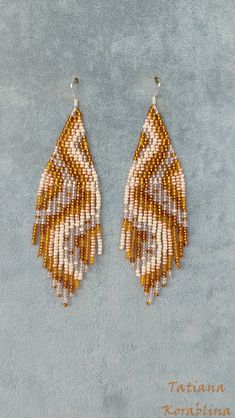 two pairs of beaded earrings with fringes on blue fabric, one in gold and the other in white