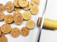 some corks and a knife on a white table with a piece of wood next to them