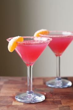 two martinis with orange garnish sit on a wooden table