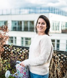 a woman standing next to a fence holding a watering can and smiling at the camera