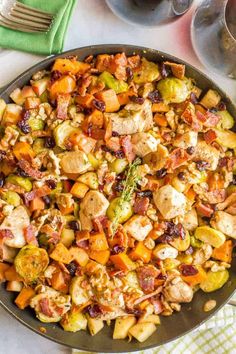 a skillet filled with stuffing and vegetables on top of a white table cloth next to wine glasses