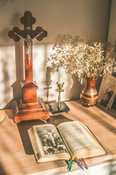 an open book sitting on top of a wooden table next to a cross and flowers