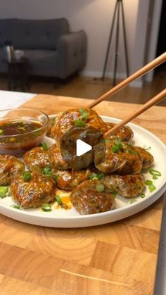 a white plate topped with meat covered in sauce and chopsticks on top of a wooden table