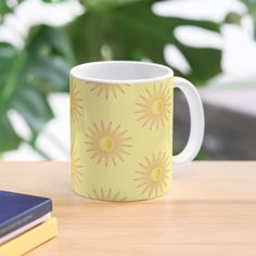 a yellow coffee mug sitting on top of a wooden table next to a book and plant