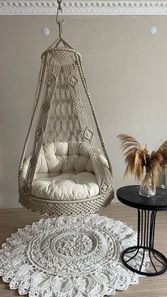 a white hanging chair next to a table with a potted plant on top of it