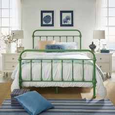 a green metal bed in a white bedroom with blue pillows and pictures on the wall