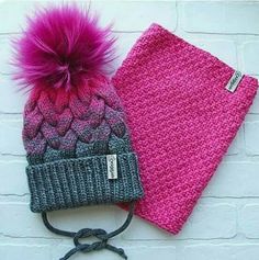 two knitted hats with pink and grey pom - poms on them next to a brick wall