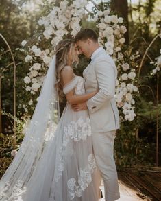 a bride and groom standing in front of an arch with white flowers on the side