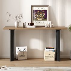 a wooden table topped with books next to a white vase filled with flowers on top of a hard wood floor