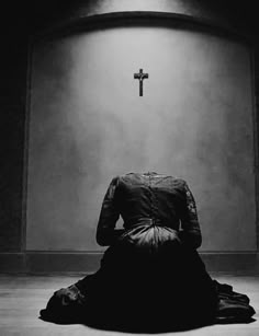 a black and white photo of a woman sitting in front of a cross