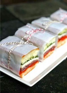 four sandwiches wrapped in white paper tied with twine on top of a small plate