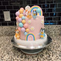 a birthday cake decorated with cartoon characters and balloons on a countertop in front of a tiled wall