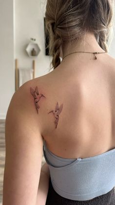 the back of a woman's shoulder with two small birds on her left arm