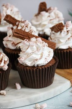 chocolate cupcakes topped with whipped cream and cinnamon sticks on a marble platter