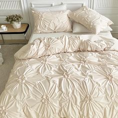 a bed with white comforter and pillows on it next to a night stand in a room