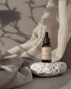 a bottle of essential oil sitting on top of a rock next to a window curtain