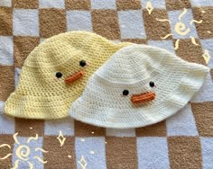 two crocheted hats sitting on top of a checkered tablecloth covered floor