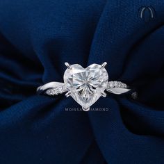 a heart - shaped diamond ring on top of a blue satin material with diamonds surrounding it