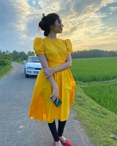 a woman standing on the side of a road wearing a yellow dress and red shoes