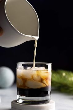 someone pouring ice into a glass filled with liquid