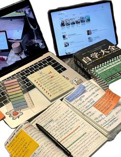 an open laptop computer sitting on top of a pile of notebooks and books next to each other