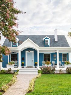 a blue and white house with flowers on the front porch, steps leading to it