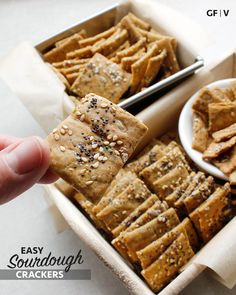 someone holding up a cracker in front of a box of crackers with sesame seeds