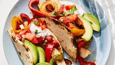 two tacos on a plate with avocado, tomatoes and other toppings