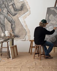 a man sitting in front of a painting on a easel next to another person