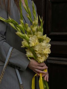 a woman holding a bouquet of yellow flowers in her hands and wearing a gray suit