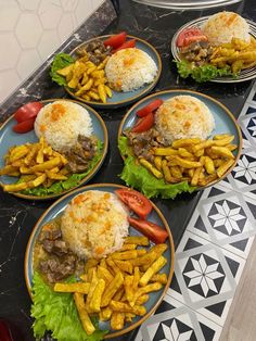 four plates filled with food on top of a black counter next to silver pans