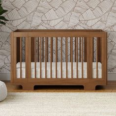 a baby crib in front of a wall with leaves on it and a plant next to it