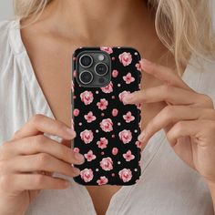 a woman holding up her phone case with pink flowers on it and black background, while she is looking at the camera