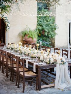 a long table with white flowers and candles is set up for an outdoor wedding reception