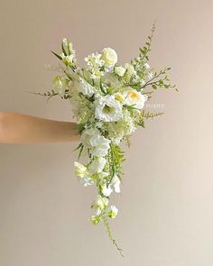 a bouquet of white and green flowers is being held up by someone's hand