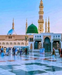 many people are walking around in front of a building with green domes and white walls