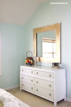 a white dresser sitting in a bedroom next to a mirror on the side of a wall