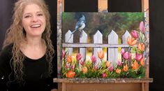 a woman standing next to an easel holding up a painting with tulips and a bird on it