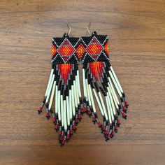 a pair of beaded earrings with red and white designs on them sitting on a wooden surface