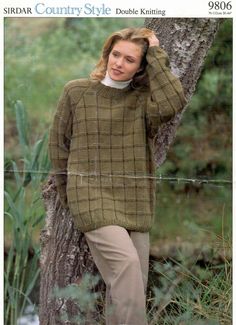 a woman standing next to a tree wearing a sweater